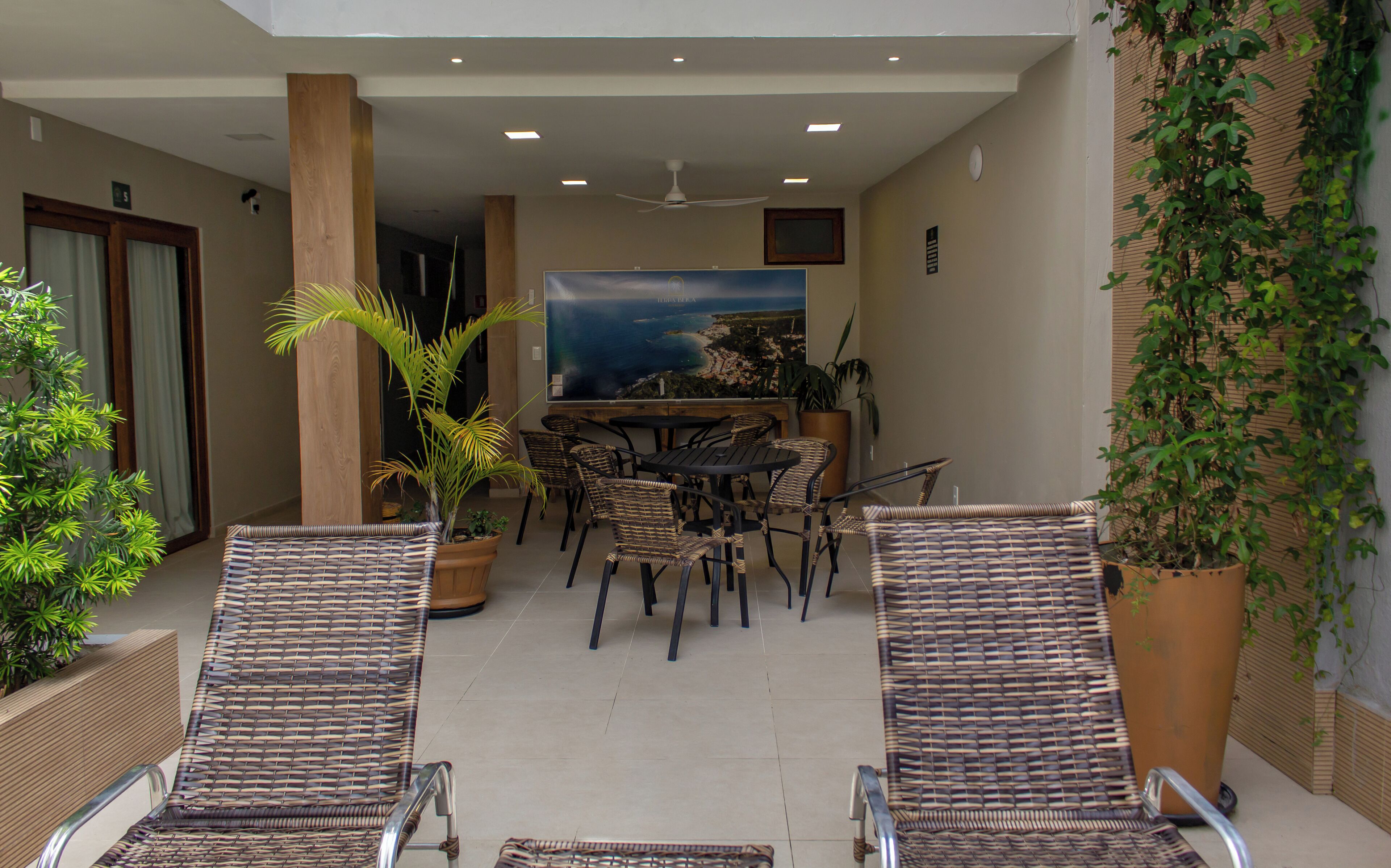 A covered outdoor seating area with wicker furniture, a large potted plant, and a view of the sea.