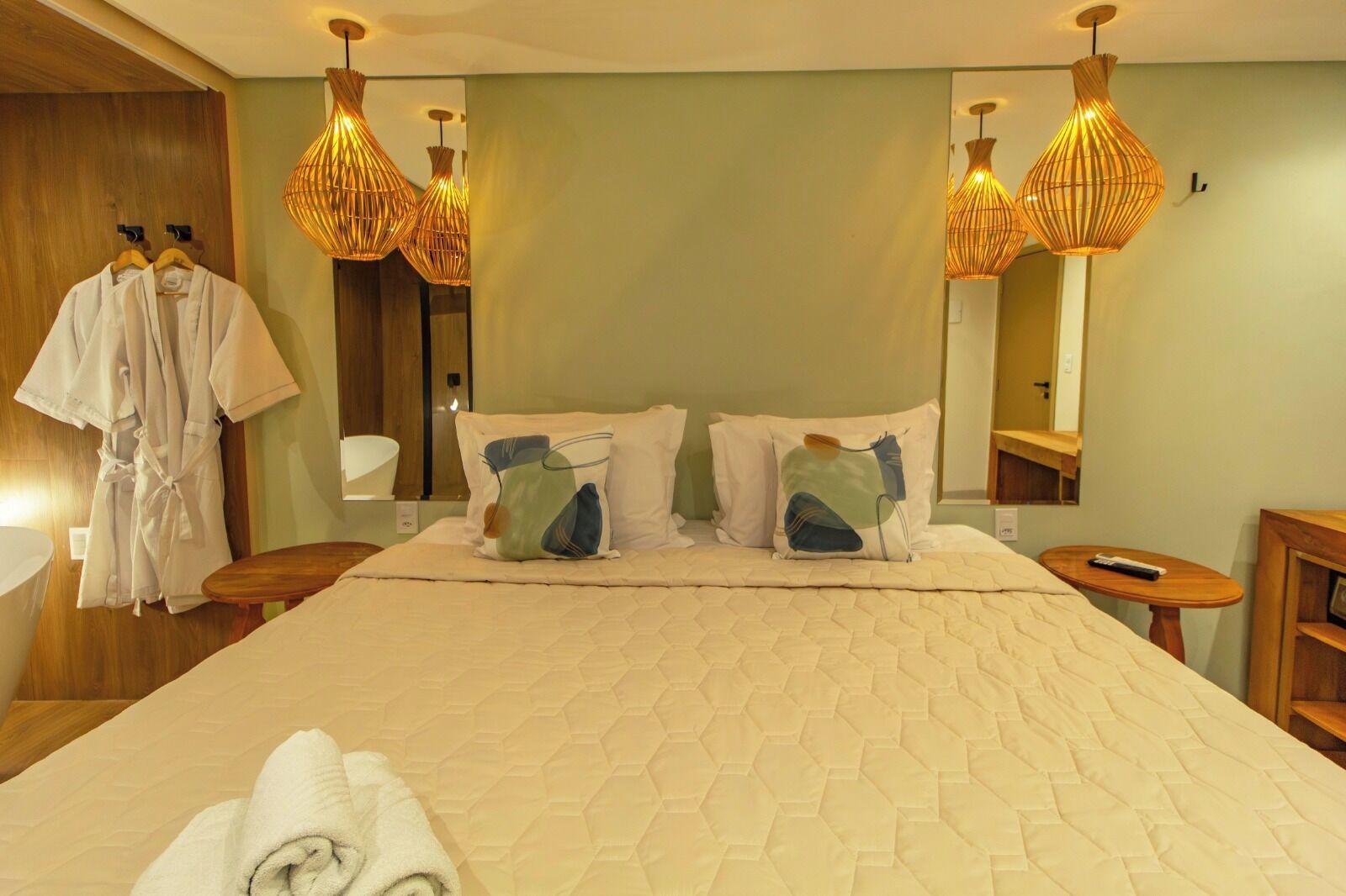 Een hotelkamer met een groot bed, twee nachtkastjes, een houten kledingkast en een spiegel.