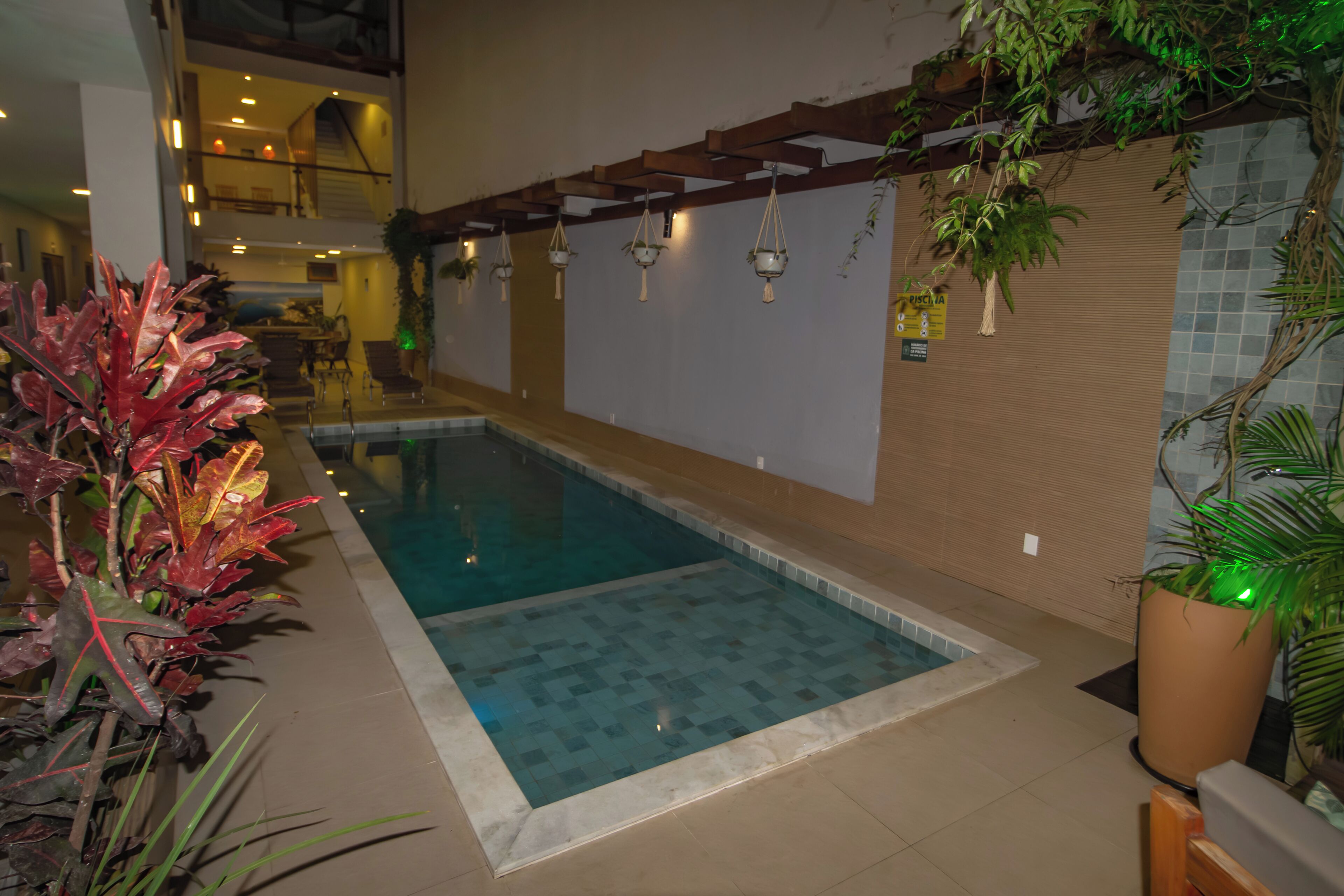 An indoor swimming pool with tiled flooring, a wooden ceiling structure, and hanging plants.