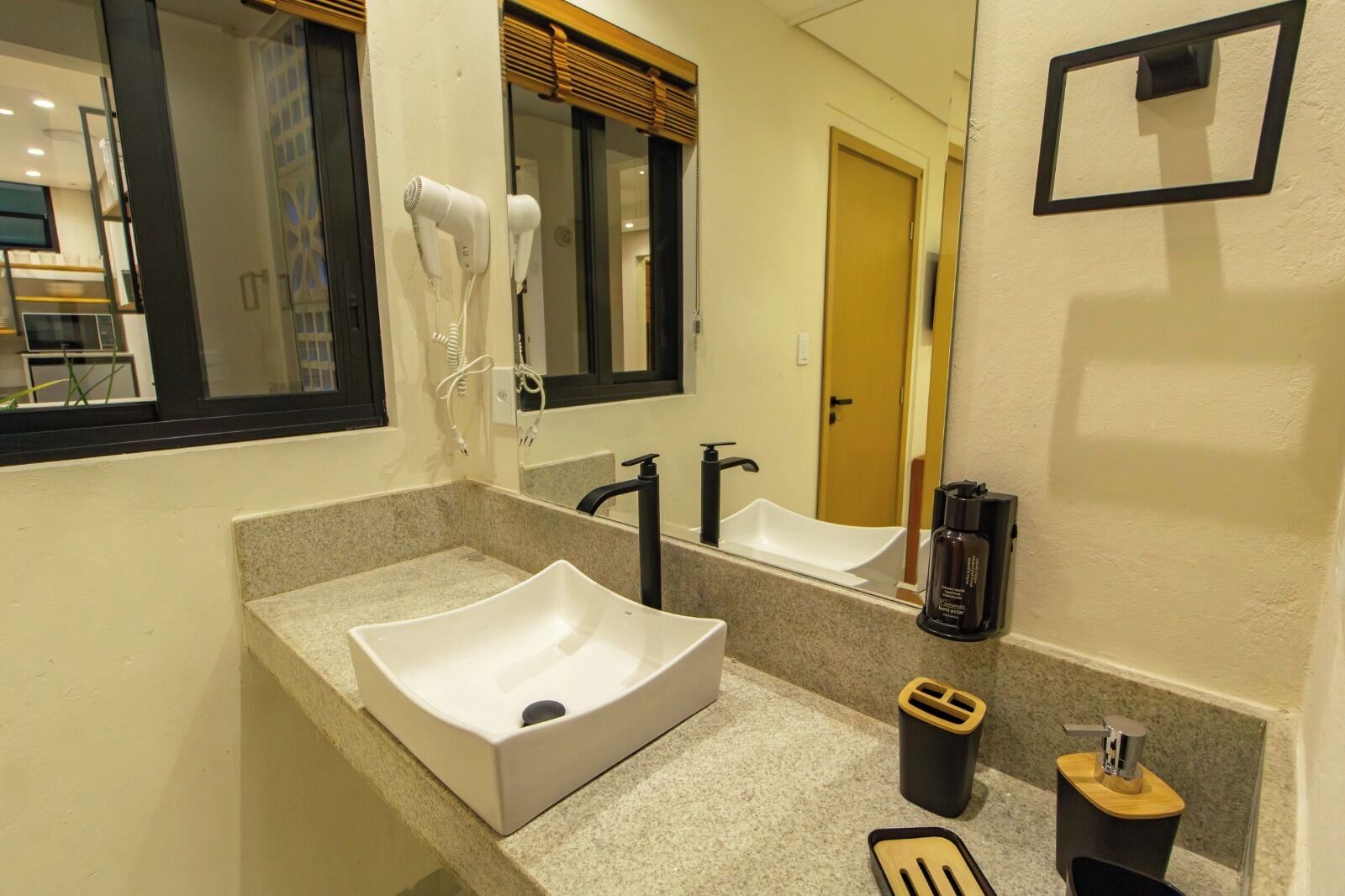 Uma casa de banho moderna com lavatório branco, espelho, secador de cabelo e máquina de café.