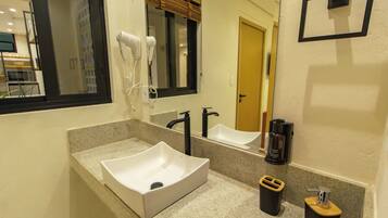 Uma casa de banho moderna com lavatório branco, espelho, secador de cabelo e máquina de café.