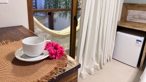 A room with a small table, a cup, a flower, a hammock, and a refrigerator. - Terra Bella Pousada (Cairu)