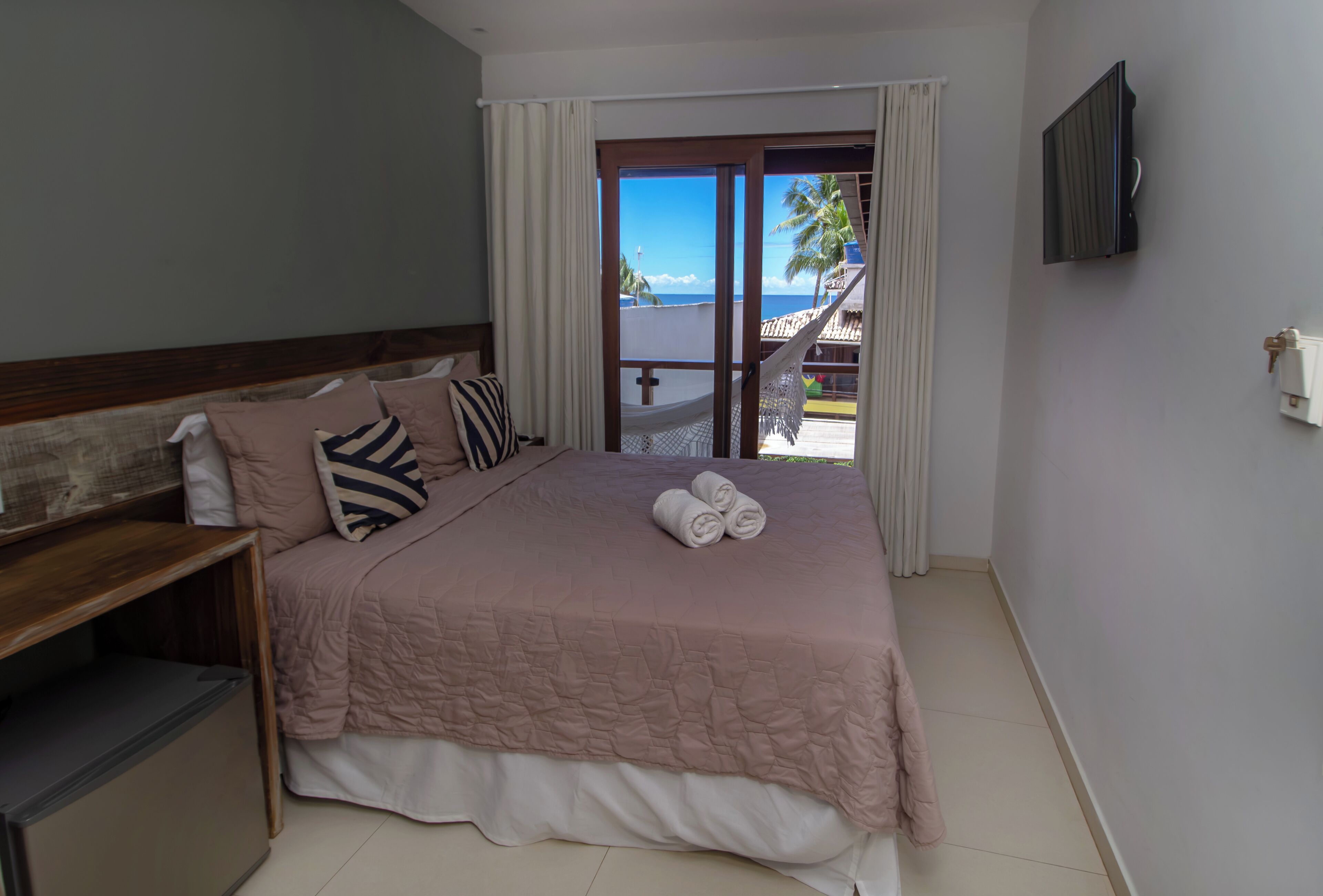 Een slaapkamer met een bed, kussens, een televisie en uitzicht op de oceaan.