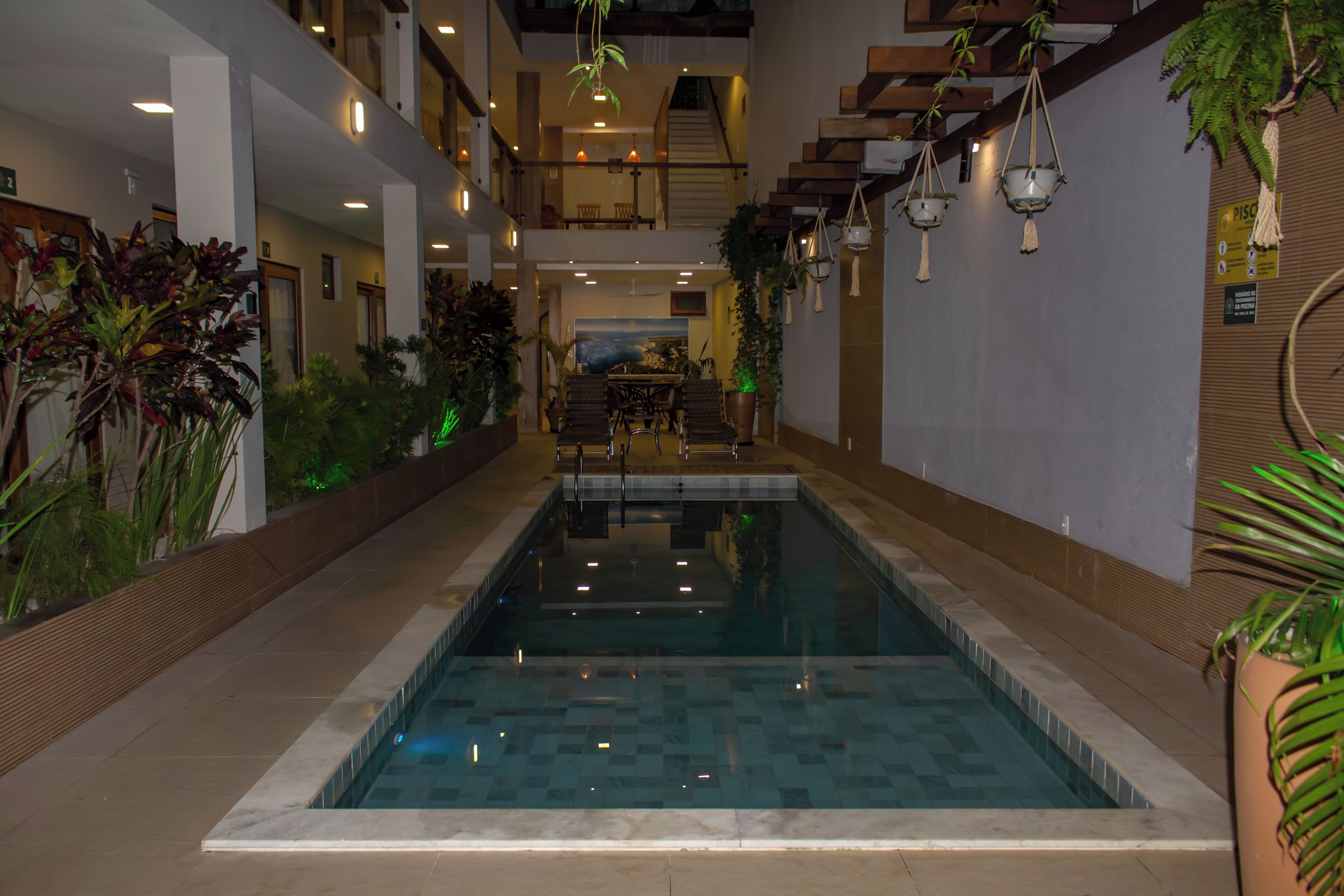 An indoor swimming pool with a view of a staircase and a dining area in the background.