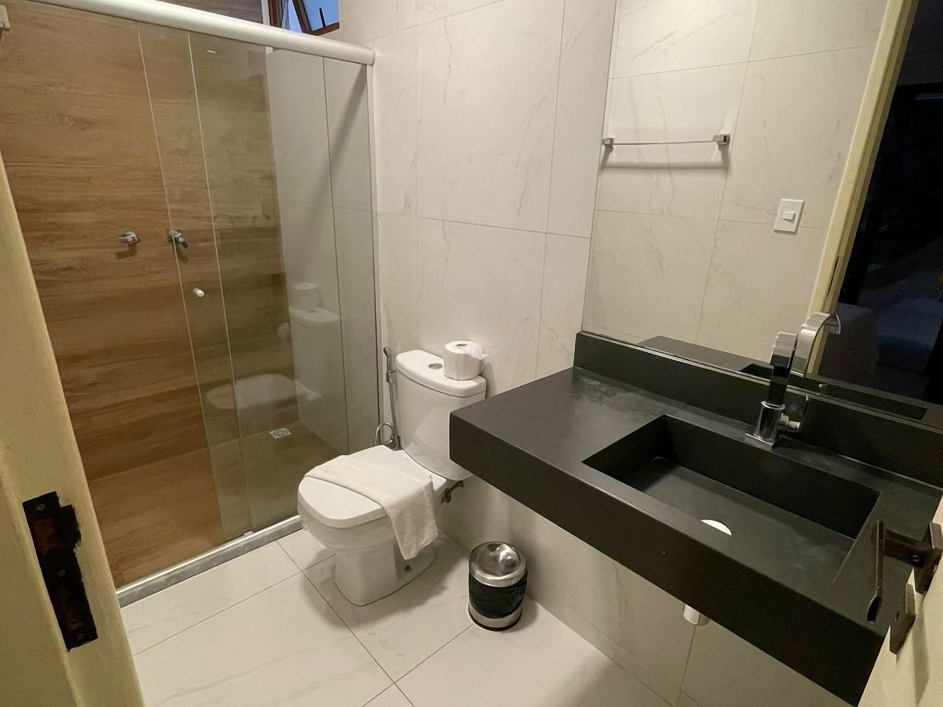 Une salle de bain moderne avec une douche à parois de verre, des toilettes, un lavabo doté d’un plan de travail foncé et un miroir.