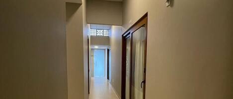 Un pasillo con suelo de baldosas, una puerta con panel de vidrio y una lámpara en el techo.