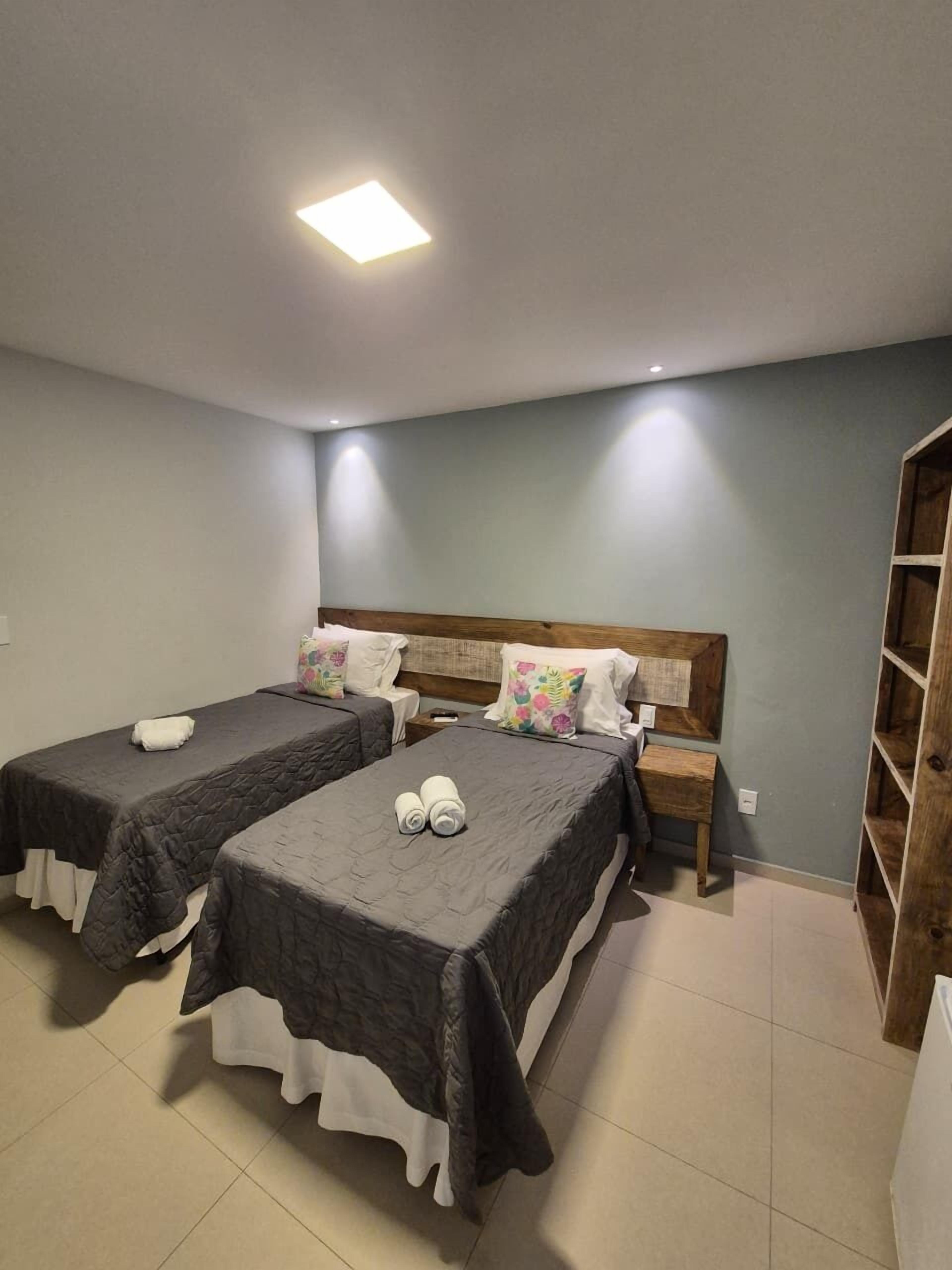 A room with two beds, a wooden headboard, bedside tables, and a built-in wooden shelf.