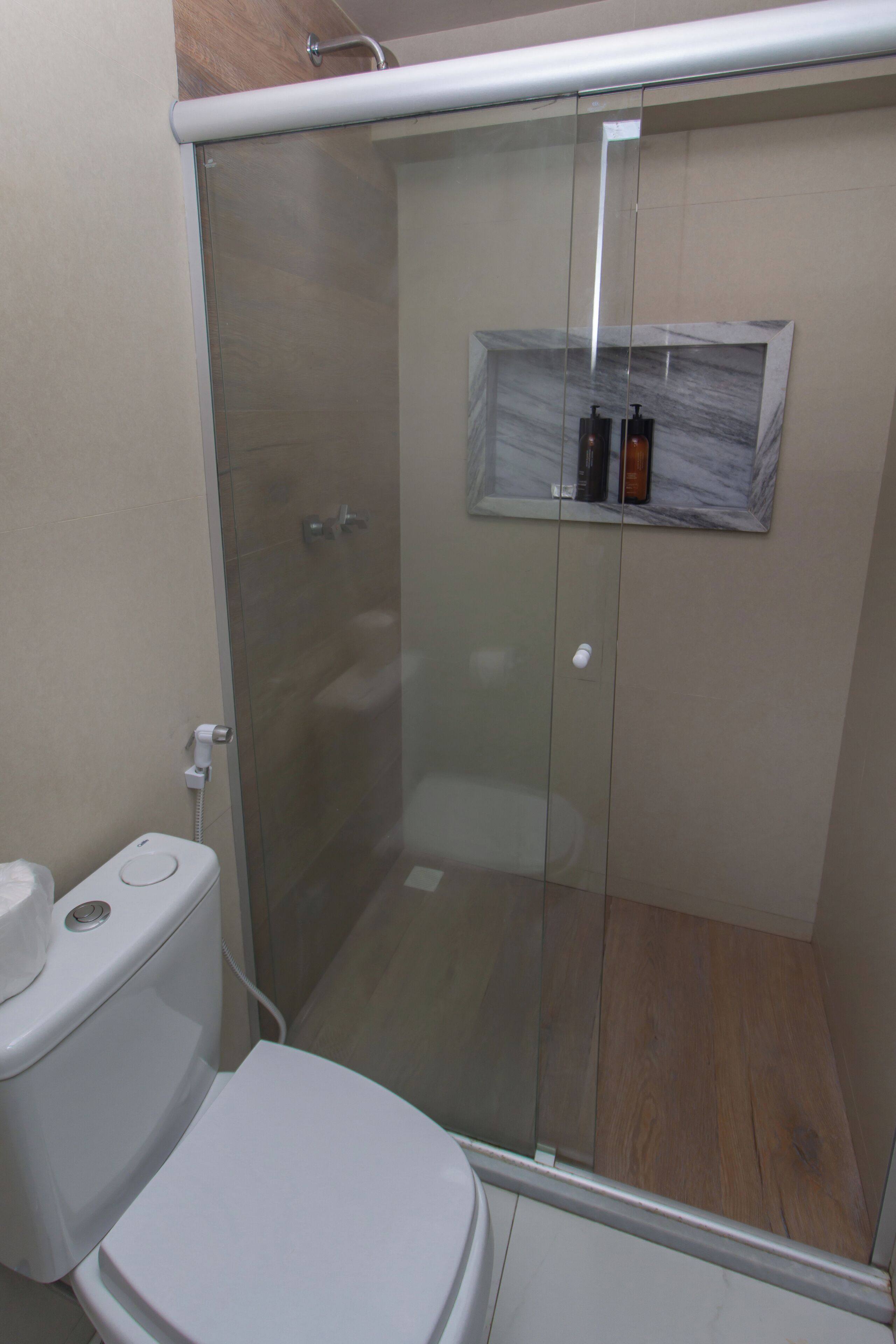 A bathroom with a glass-enclosed shower, a toilet, and a marble shelf with toiletries.