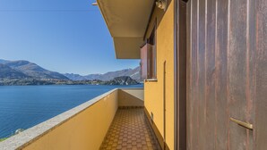 En balkon med flisegulv, en gul væg og en trædør. Der er frit udsyn til en sø og bjerge i baggrunden.