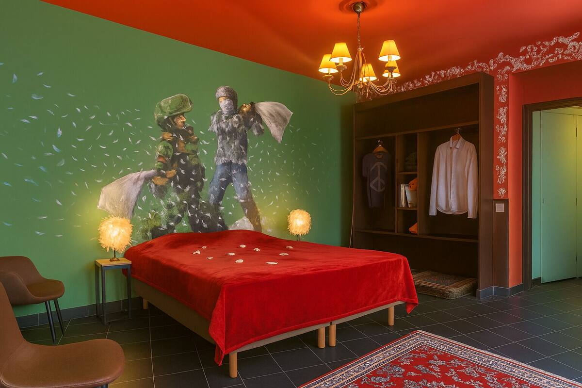 A bedroom with a bed, a chair, a wardrobe, and a wall mural.