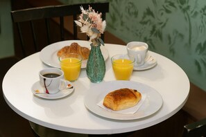 Desayuno con cruasanes, café, jugo de naranja y un florero decorativo sobre una mesa redonda.