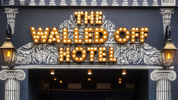El exterior del Hotel The Walled Off, con un llamativo letrero iluminado, columnas y una entrada oscura.