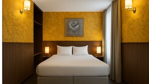 Habitación de hotel con una cama grande, dos mesitas de noche con lámparas, una obra de arte colgada en la pared y una cortina en la ventana.