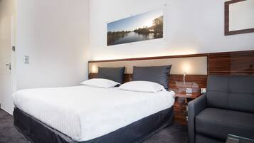 A hotel room with a large bed, a bedside table, a chair, and a framed picture on the wall.