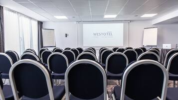 Una sala de conferencias con filas de sillas, una pantalla de proyector mostrando