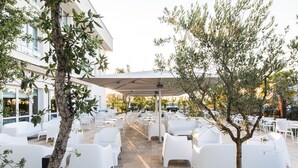 Een terras met witte stoelen en tafels, een pergola en een gebouw op de achtergrond.