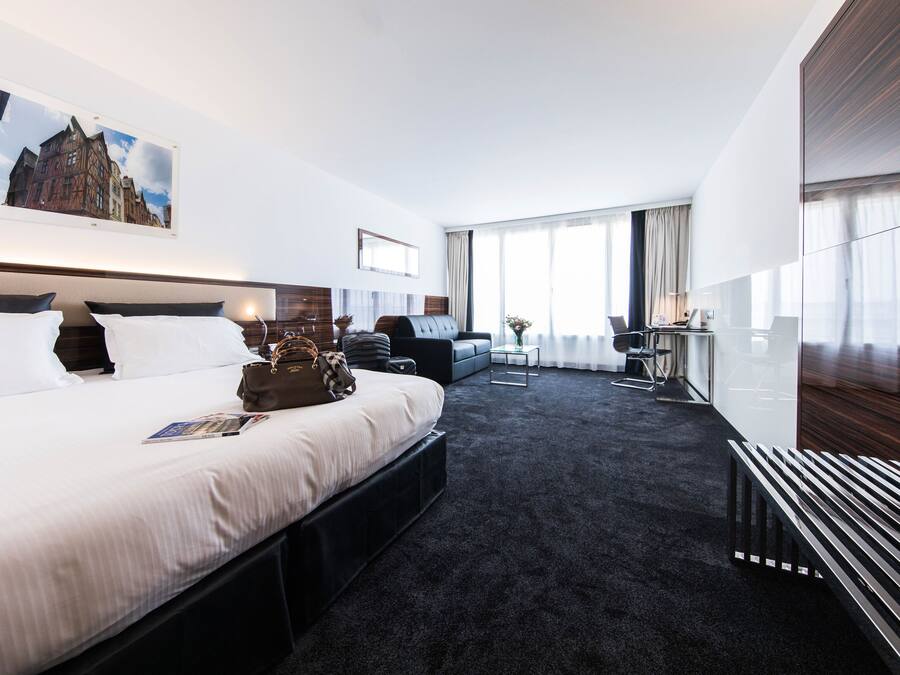 Een moderne hotelkamer met een groot bed, een bureau, een stoel, een bank en uitzicht op de stad.