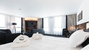 Een moderne hotelkamer met een groot bed, twee fauteuils, een bureau met stoel en een televisie.