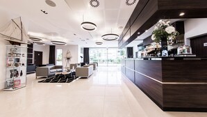 Een moderne hotel lobby met een receptiebalie, een zithoek en een groot raam met uitzicht op de stad.