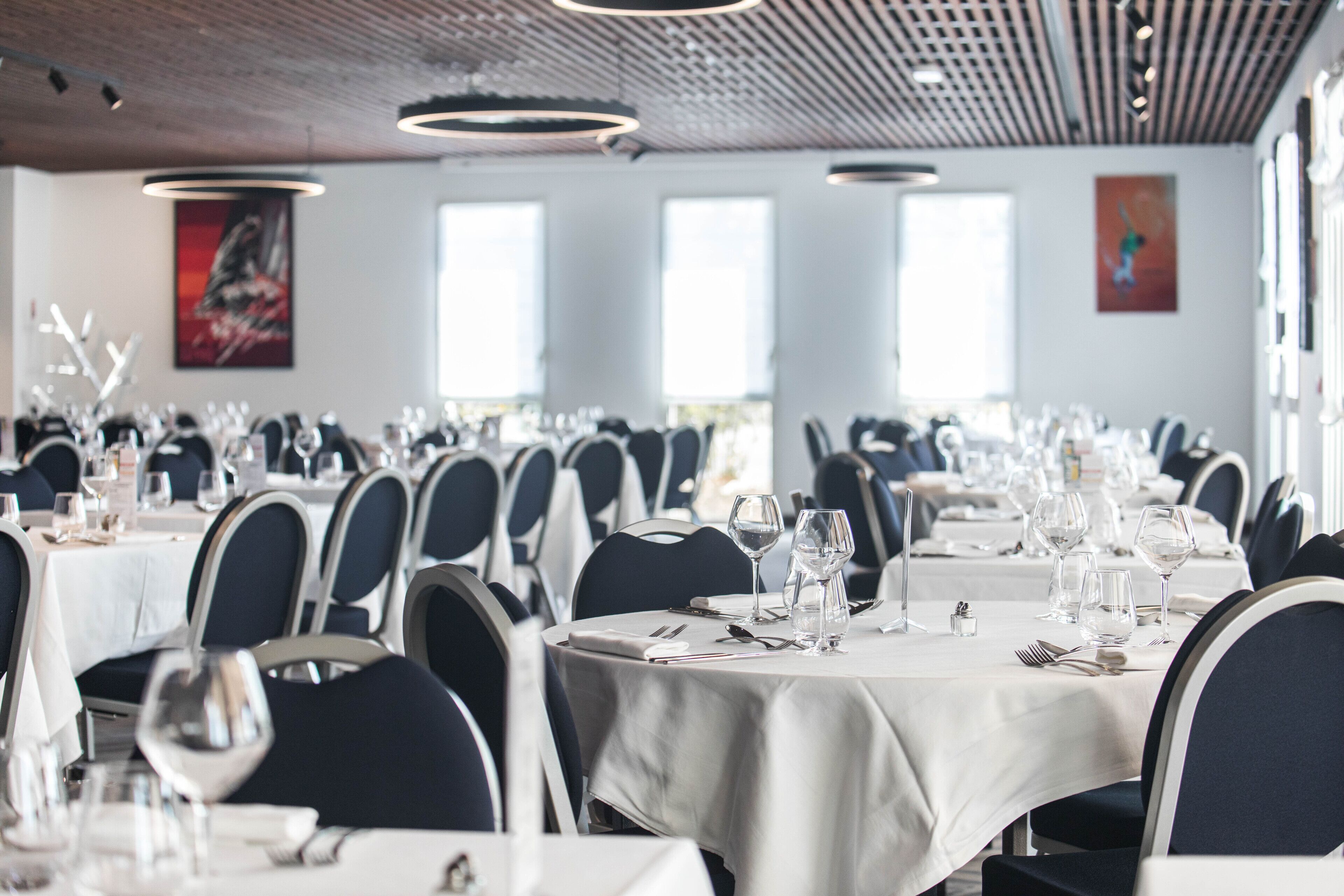 Un restaurante con mesas redondas, sillas oscuras y manteles blancos.
