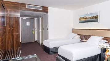 Habitación de hotel con dos camas, un escritorio con teléfono, un cuadro en la pared y una puerta que da a otra habitación.