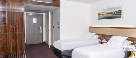 A hotel room with two beds, a desk with a phone, a painting on the wall, and a door leading to another room.