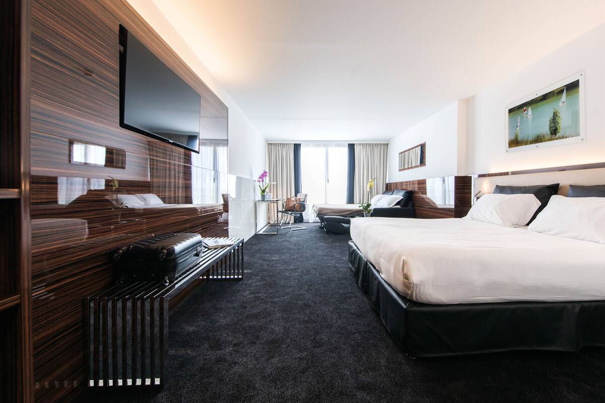 Ein modernes Hotelzimmer mit einem großen Bett, einem Schreibtisch, einem Flachbildfernseher und einem Fenster mit Vorhängen.