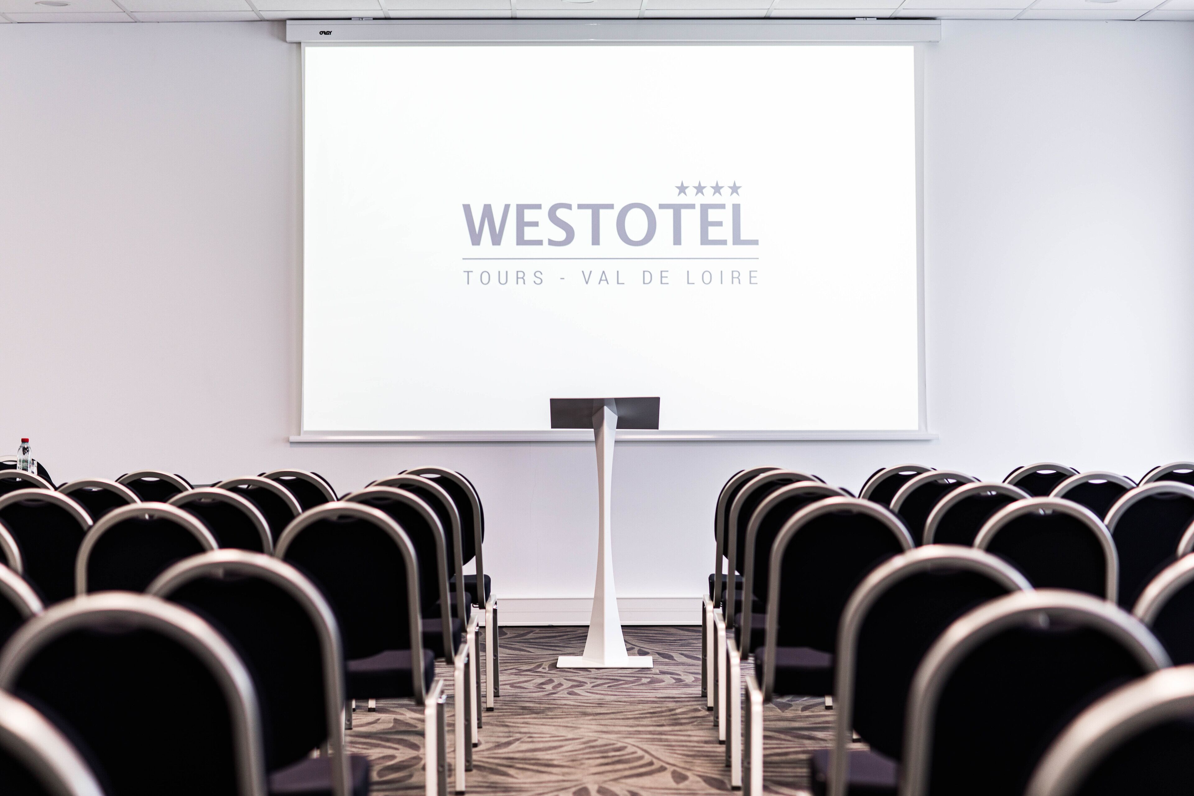 A conference room with rows of chairs facing a projection screen displaying "WESTOTEL TOURS - VAL DE LOIRE".