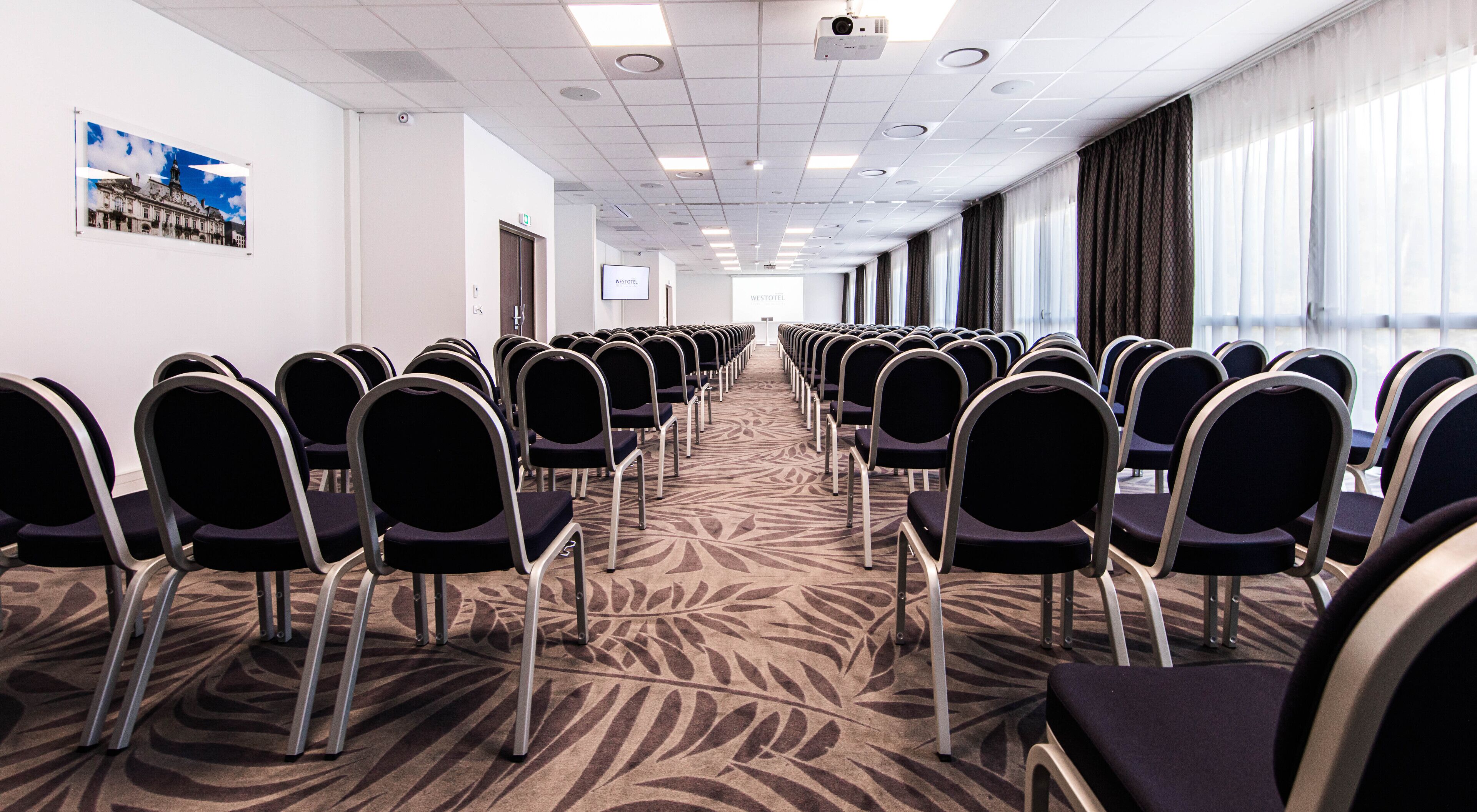 Une salle de conférence avec des rangées de chaises et un sol recouvert de moquette.