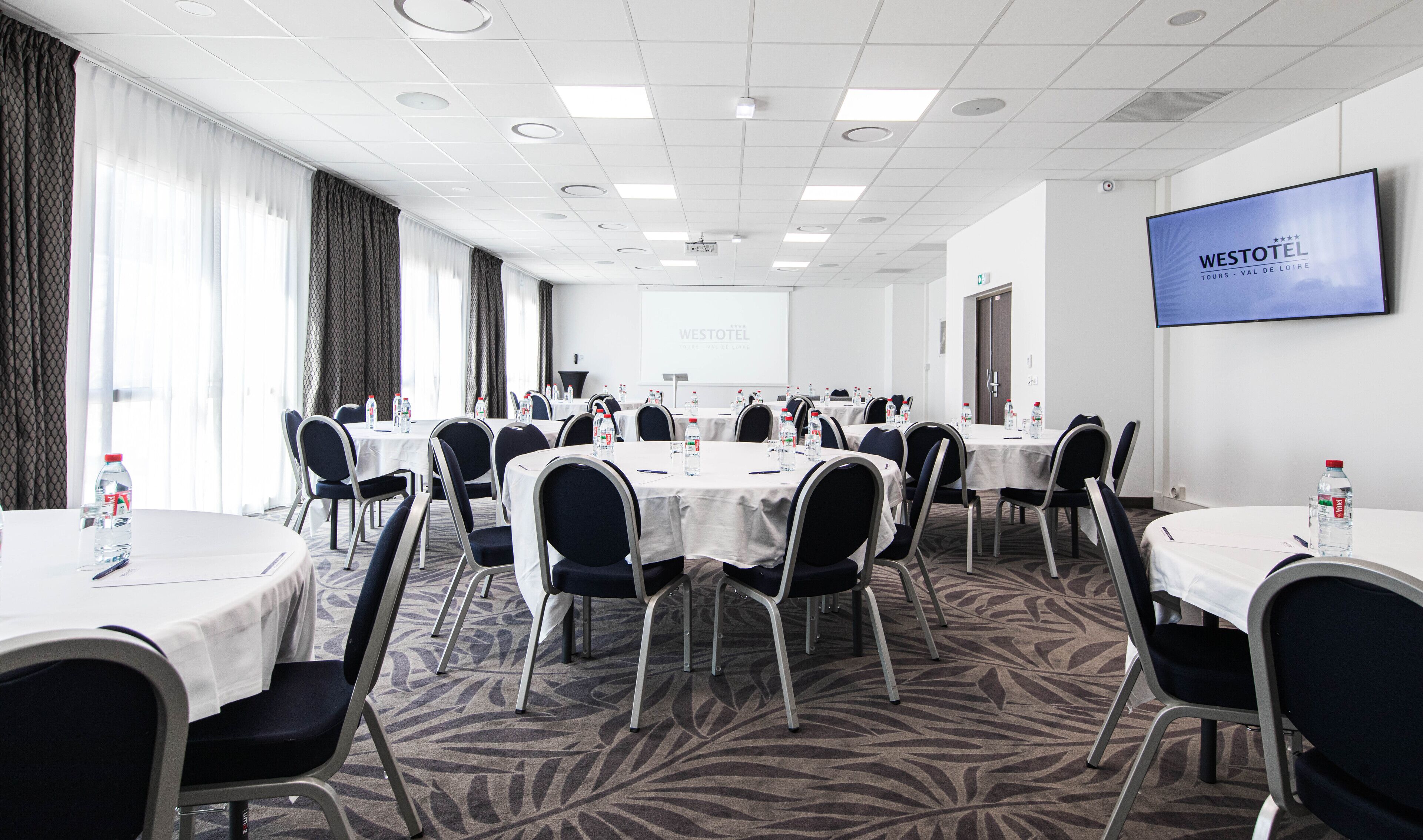 A conference room with round tables, chairs, and a projector screen displaying 'WESTOTEL'.
