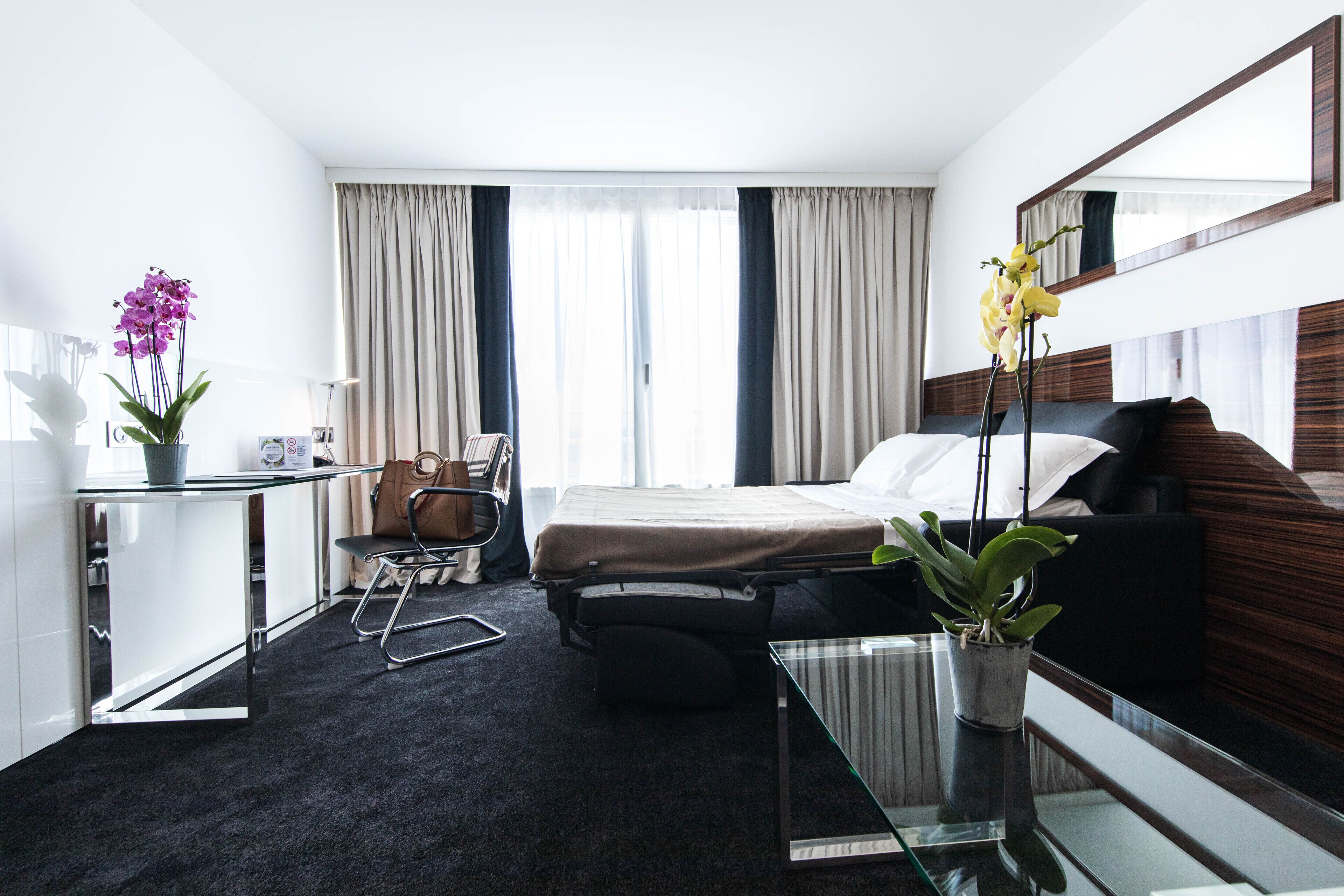 Habitació d'hotel moderna amb un llit, escriptori, cadira, taula petita i una planta en test.