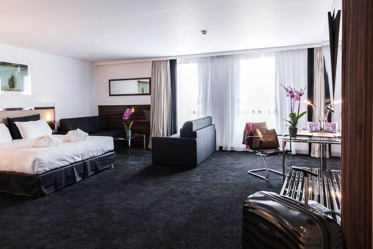 Ein Hotelzimmer mit Bett, einer Sitzecke, einem Schreibtisch mit Stuhl und einem Gepäckträger.