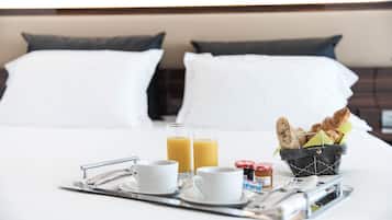 Ein schön gedecktes Frühstücksbrettchen mit zwei Orangensäften, zwei weißen Tassen, einem Marmeladenglas und einem Korb mit Croissants auf einem Hotelbett.