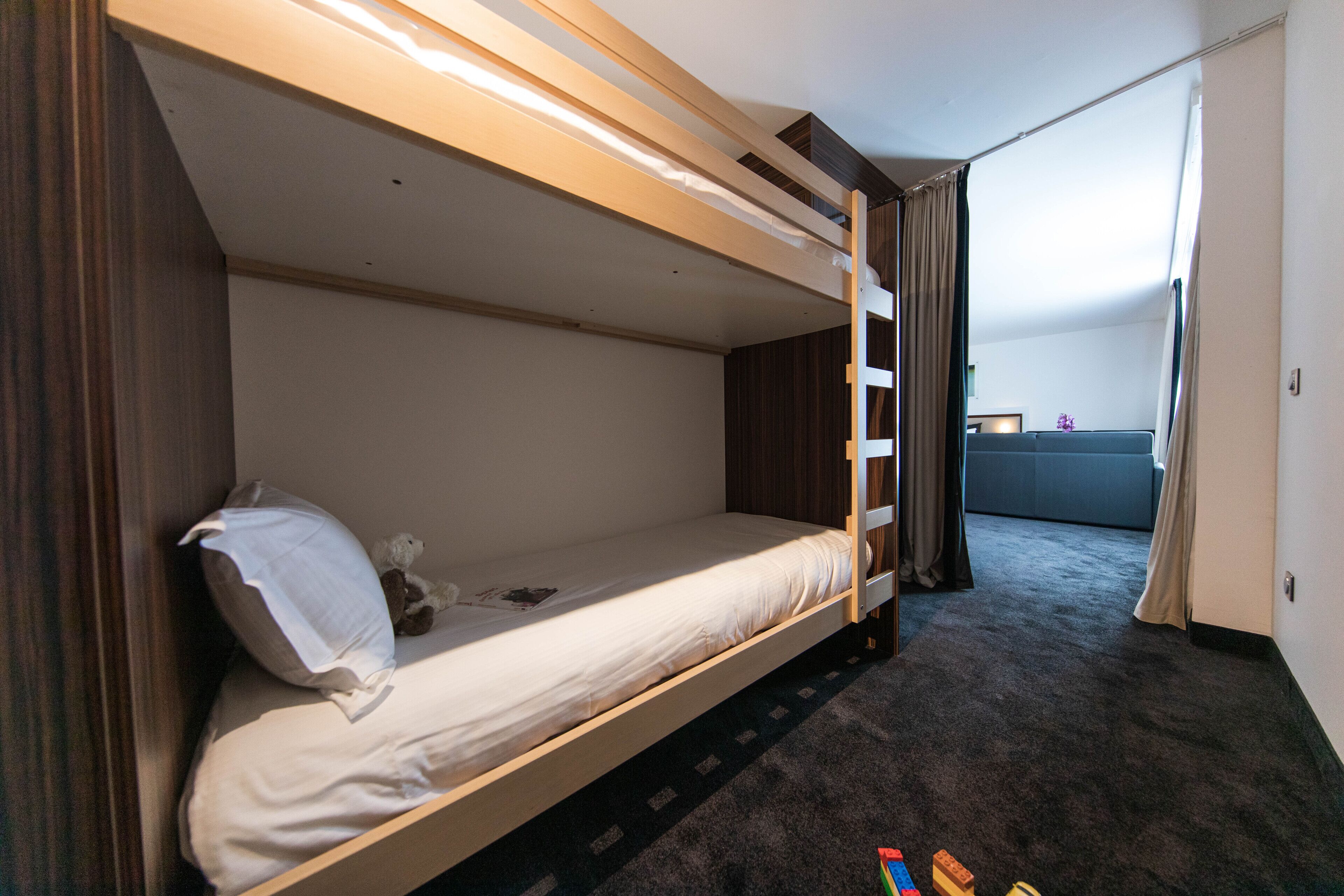 Habitación con literas, una mesita pequeña, una silla, una ventana con cortinas y suelo alfombrado.