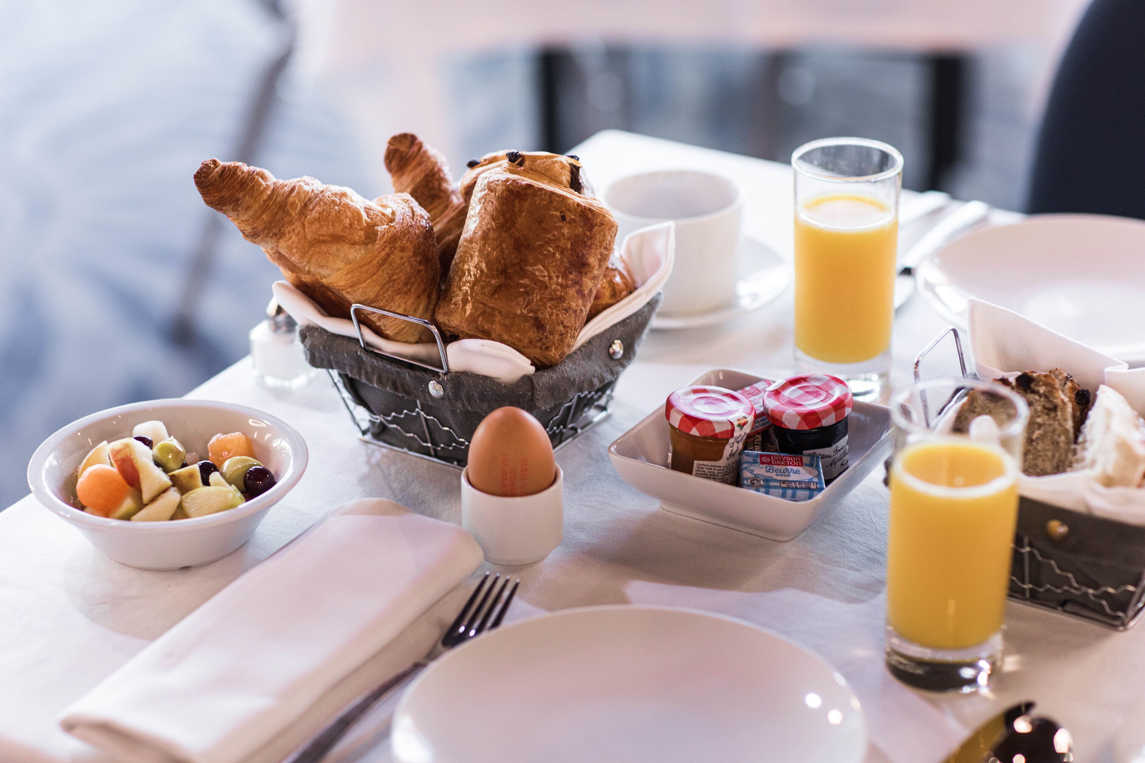 Een ontbijttafel met croissants, fruit, een glas sinaasappelsap en toevoegingen.