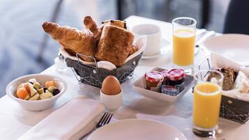 Une table de petit-déjeuner avec des croissants, des fruits, un verre de jus d’orange et des condiments.