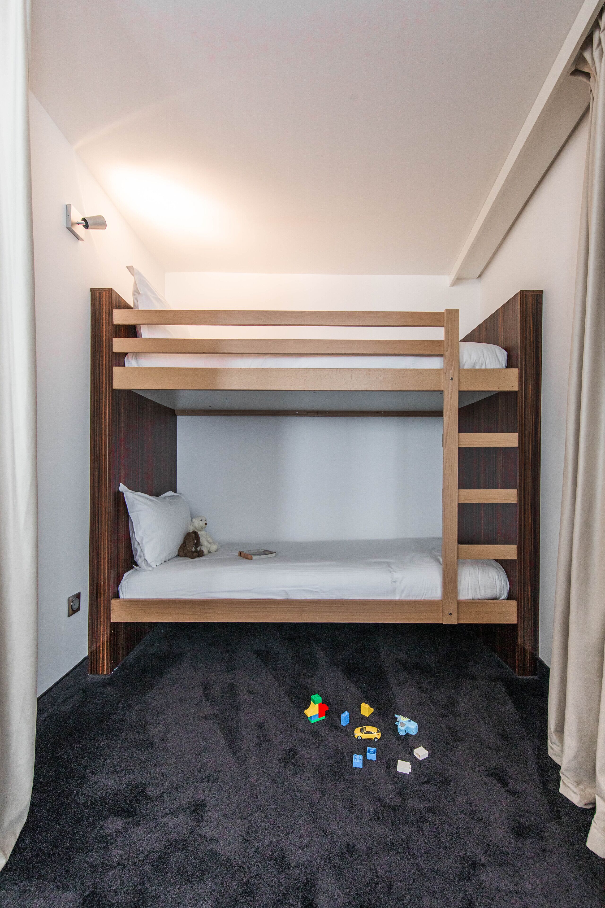 A bunk bed room with a dark carpet and toys scattered on the floor.
