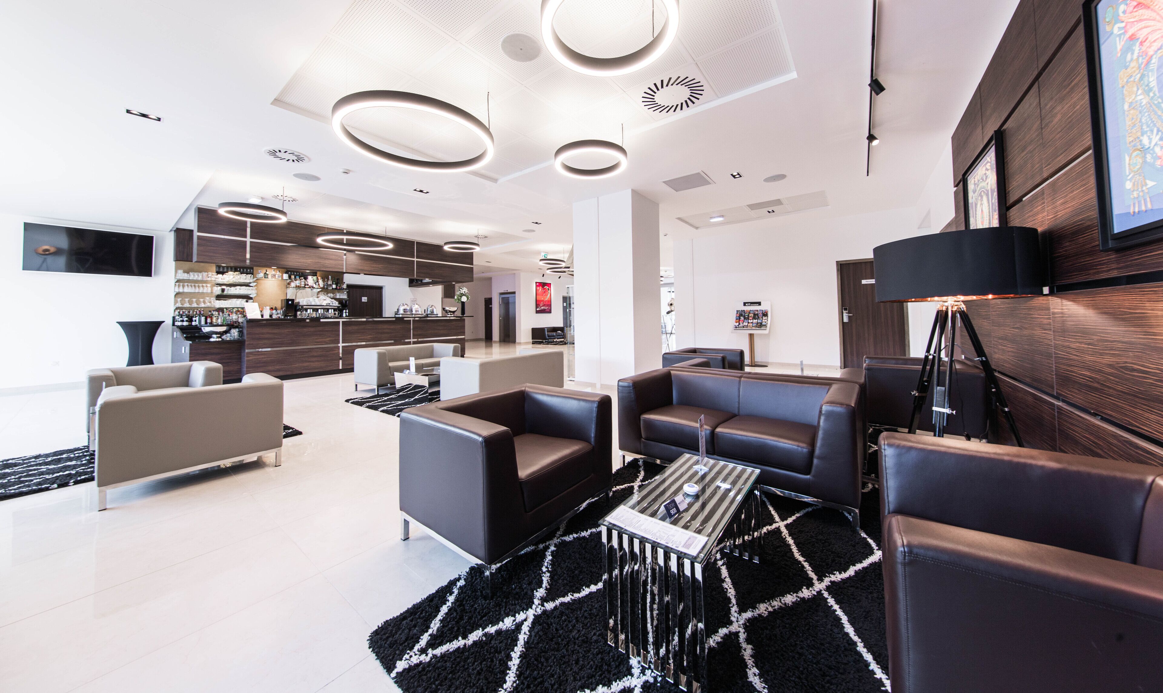 A modern hotel lobby with a bar area, seating arrangements, and a large screen.