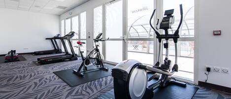 A hotel gym with treadmills, an elliptical, and a stationary bike, all on mats.