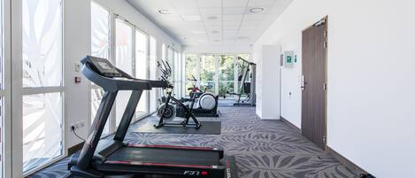 Un gimnasio con cintas de correr y bicicletas estáticas, ventanas amplias y una alfombra estampada.