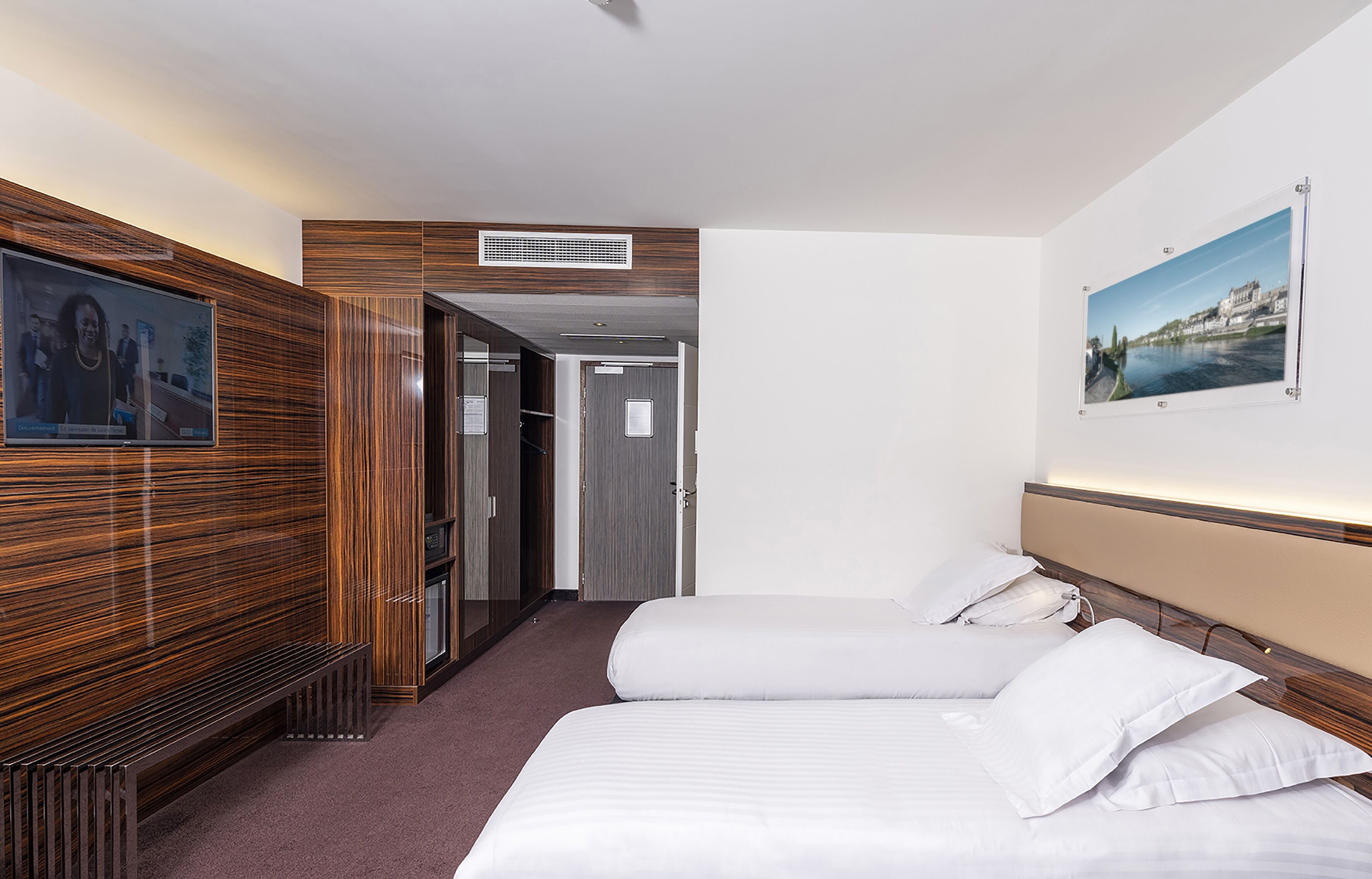 Une chambre d’hôtel avec deux lits, une télévision, un mur recouvert de panneaux de bois et un tableau encadré.
