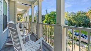 A covered porch with a white chair, a view of the street, and greenery in the background.