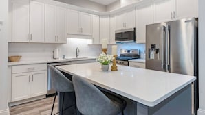 A modern kitchen with white cabinetry, stainless steel appliances, and a central island with bar stools.