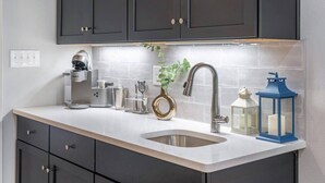 A modern kitchen with dark cabinets, a stainless steel sink, a coffee machine, and decorative items.
