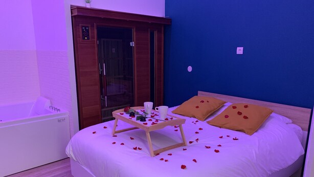 Quarto de hotel com cama, uma mesinha com um tabuleiro de objetos, banheira e guarda-roupa de madeira.