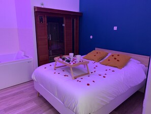 Une chambre d’hôtel avec un lit, une petite table sur laquelle se trouve un plateau avec divers objets, une baignoire et une armoire en bois.