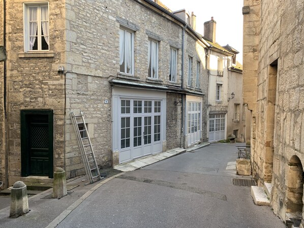 A narrow street with stone buildings, a visible garage door, and a ladder leaning against a wall.