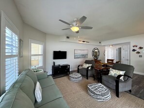 A living room with a ceiling fan, a flat-screen TV, a dining table with chairs, and a sofa.