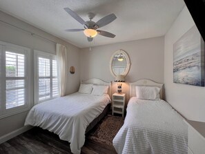 A bedroom with two beds, a ceiling fan, a nightstand with a lamp, a mirror, and a window with blinds. - Inviting 2BR Condo in Prime Destin Location (Destin)