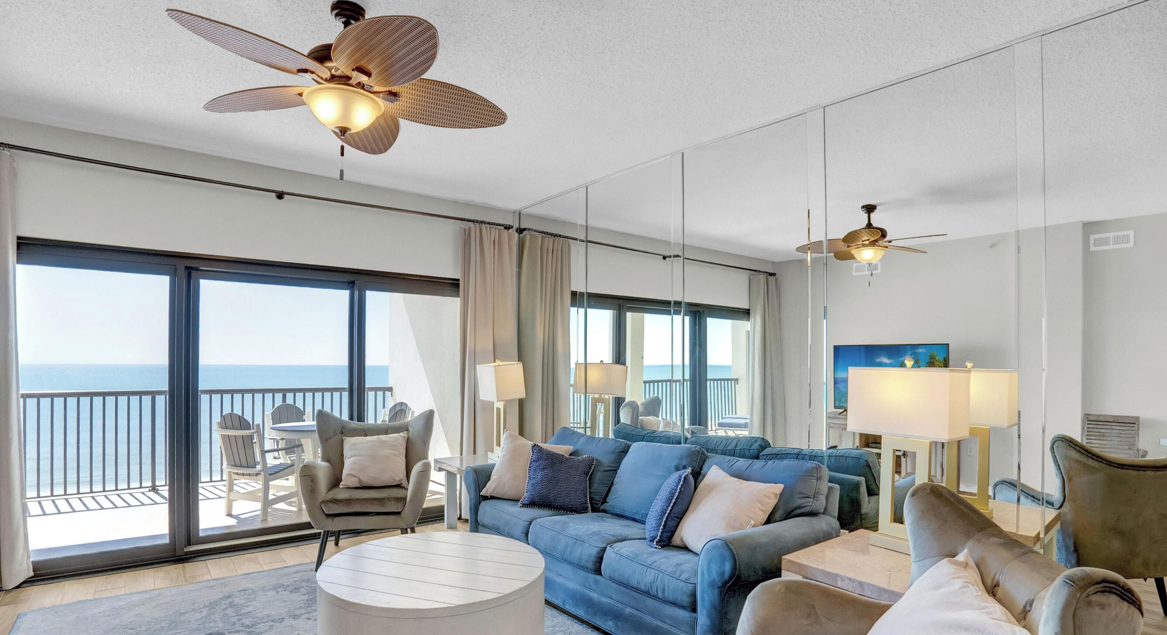 Une chambre d’hôtel avec un balcon, un canapé, une table basse et deux ventilateurs de plafond.